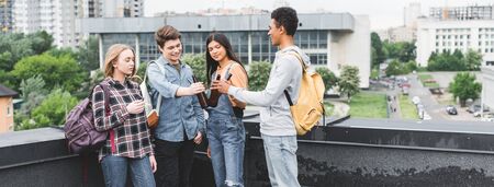 Panoramic shot of smiling teenagers clinking and smoking cigaretteの写真素材