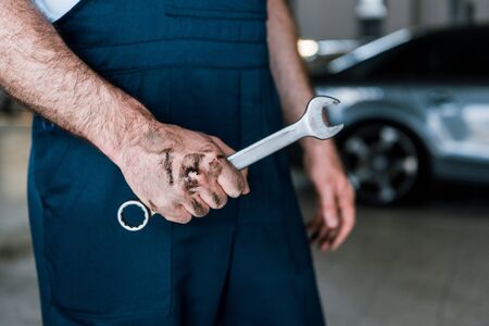 Cropped view of auto mechanic with mud on hand holding hand wrench in car repair stationの写真素材