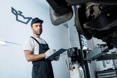Selective focus of car mechanic holding clipboard while looking at car