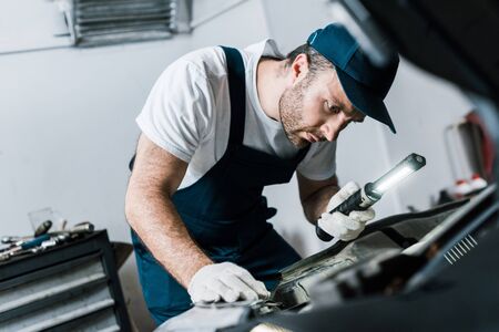 Selective focus of bearded car mechanic holding flashlight near carの写真素材