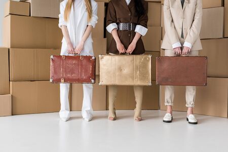 cropped view of girls standing with suitcases near boxes on whiteの写真素材
