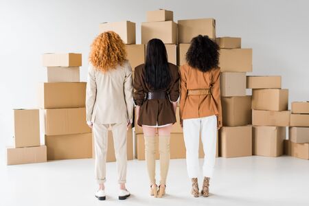 back view of redhead girl standing with stylish african american women near boxes on whiteの写真素材