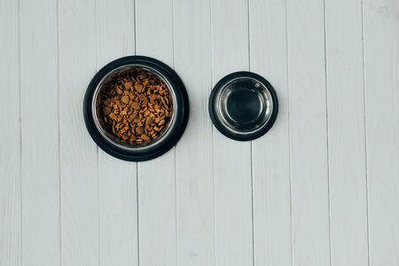 top view of bowl with pet food and empty bowl on wooden surface with copy space