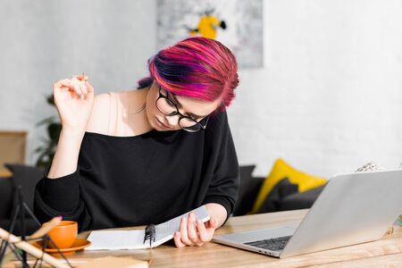 girl with colorful hair sitting at table and writing notes in notebookの写真素材