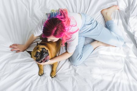 top view of girl with colorful hair sitting in bed with dogの写真素材
