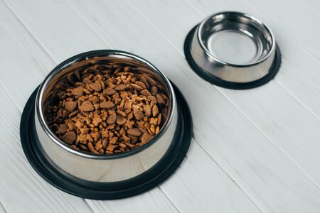 metal bowl with pet food and empty bowl on white wooden surfaceの写真素材