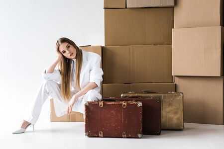 attractive blonde woman posing near suitcases and carton boxes on white