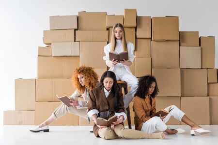 multicultural girls sitting near boxes and reading books on whiteの写真素材