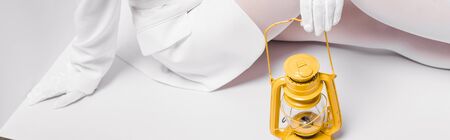 panoramic shot of young woman sitting with yellow retro lamp on whiteの写真素材