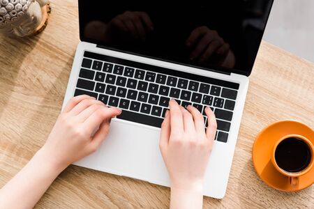 cropped view of woman using laptop on table near cup of coffeeの写真素材