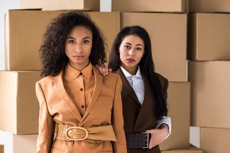 stylish african american women looking at camera near cardboard boxesの写真素材