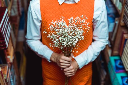 cropped view of woman in orange dress holding white flowers in libraryの写真素材