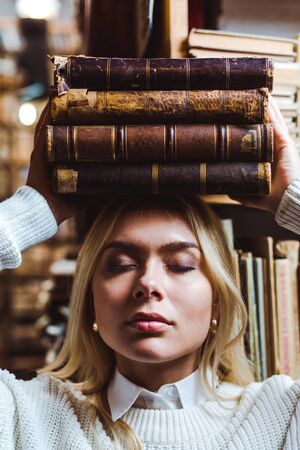blonde and pretty woman with closed eyes holding books in libraryの写真素材