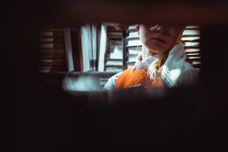 selective focus of blonde woman in glasses in libraryの写真素材