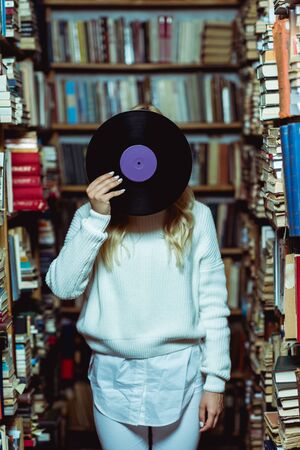 young adult woman in white sweater holding vinyl in libraryの写真素材