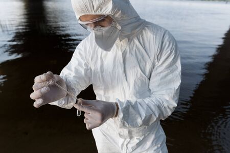 partial view of water inspector in respirator and goggles taking water sample