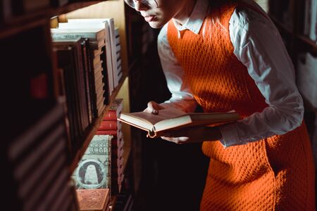 cropped view of woman in orange dress holding book in library