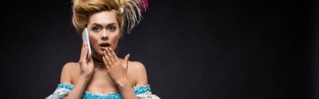 panoramic shot of surprised victorian woman talking on smartphone on black