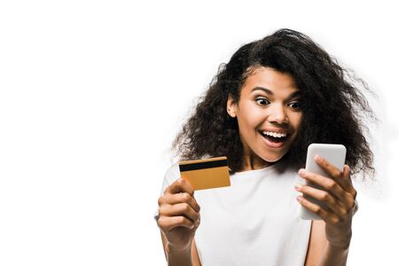 cheerful african american woman holding credit card and looking at smartphone isolated on whiteの写真素材