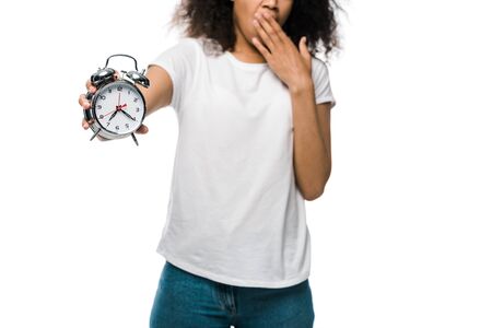 selective focus of vintage alarm clock in hand of african american girl covering mouth isolated on whiteの写真素材