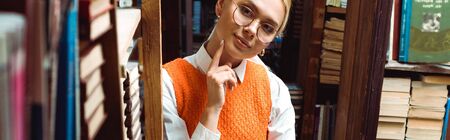 panoramic shot of pretty and blonde woman in glasses looking away in libraryの写真素材