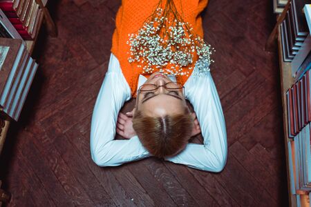 high angle view of beautiful woman lying on wooden floor with white flowers in library