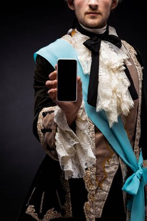 cropped view of victorian man holding smartphone with blank screen on black