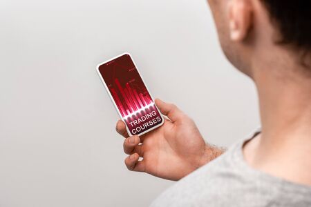 cropped view of man using smartphone with trading courses app, isolated on grey