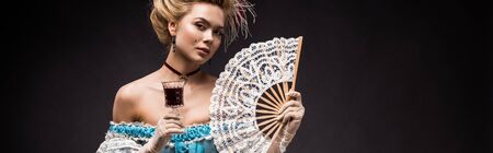 panoramic shot of victorian woman holding fan and wine glass on blackの写真素材