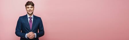 panoramic shot of handsome, cheerful businessman smiling at camera on pink background