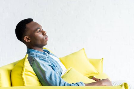 side view of calm african american man sitting on couch at homeの写真素材