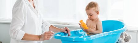 panoramic shot of mother near cute toddler son holding bottle with shampoo