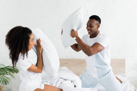 african american couple fighting on bed with pillows in handsの写真素材