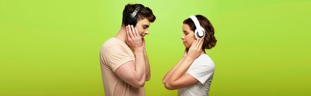 panoramic shot of positive man and woman in headphones listening music with closed eyes on green backgroundの写真素材