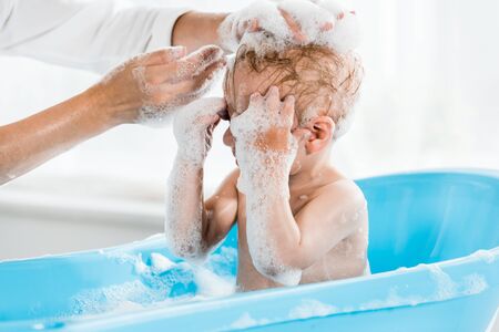 cropped view of mother washing head of toddler son in bathroom