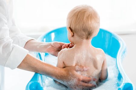 cropped view of woman washing toddler child in baby bathtub