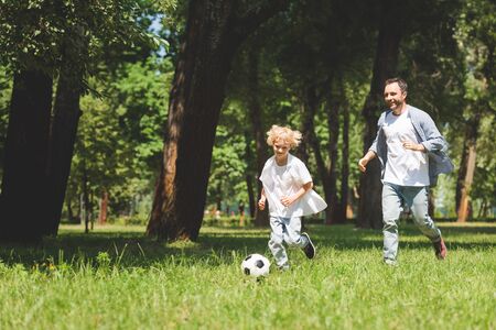 father and adorable son playing football with soccer ball in park with copy spaceの写真素材