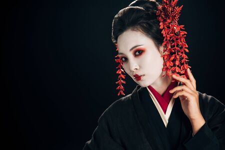 beautiful geisha in black and red kimono and flowers in hair isolated on black with copy space