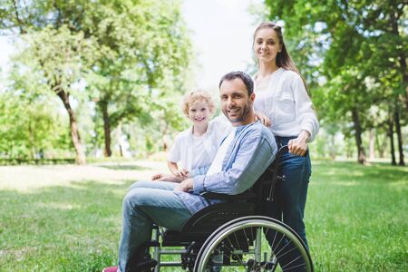 happy mother and son with disabled father on wheelchair in park