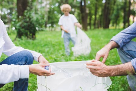 partial view of family picking up garbage in plastic bag in parkの写真素材