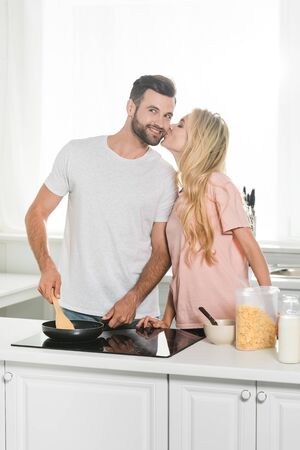 woman kissing man cooking breakfast at kitchenの写真素材