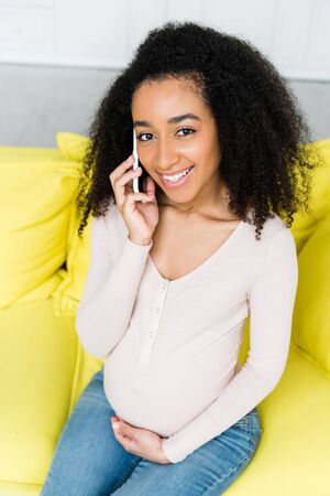 high angle view of happy and pregnant african american woman talking on smartphone