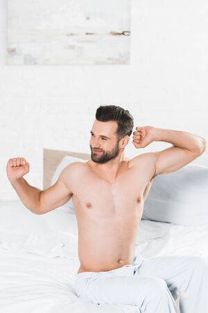handsome man stretching on bed during morning in bedroomの写真素材