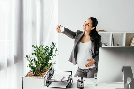 pregnant woman standing near table and flowerpot, and taking selfieの写真素材
