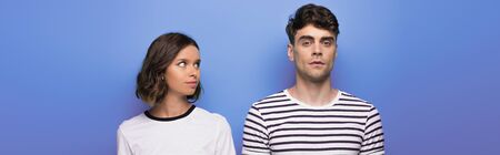 panoramic shot of positive young girl looking at offended boyfriend on blue background