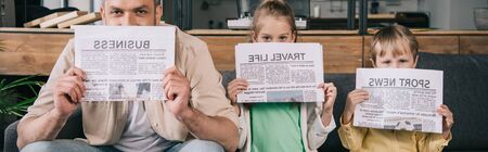 panoramic shot of cheerful father and kids covering faces with newspapers