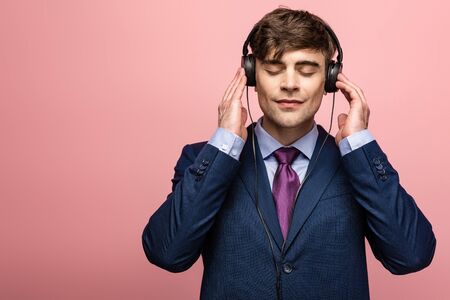 pensive smiling man listening music in earphones with closed eyes on pink background