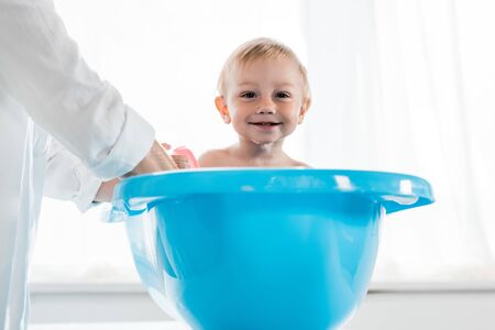 cropped view of mother washing happy toddler child in blue baby bathtubの写真素材