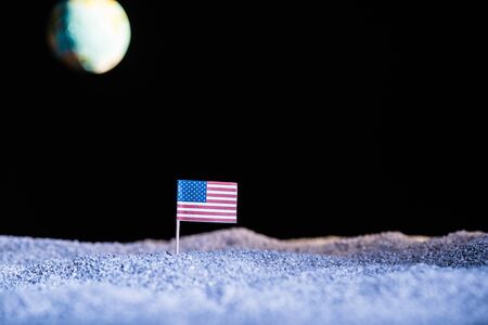 sandy ground with american flag and blurred planet Earth in space isolated on blackの写真素材