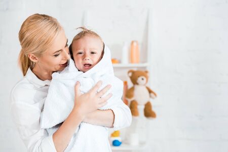 attractive blonde mother holding in arms upset toddler son in bathroomの写真素材